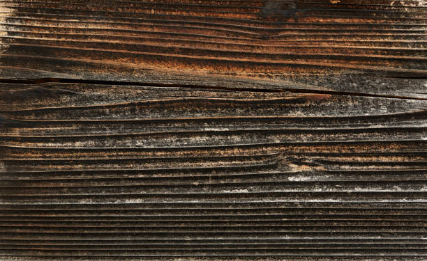 Weathered and scratched rustic wooden board.High angle view of a flat textured wooden board backgrounds. It has a beautiful nature and abstractive pattern. A close-up studio shooting shows details and lots of wood grain on the wood table. The piece of wood at the surface of the table also appears rich wooden material on it. The wood is dark brown color with darker brown lines and pattern on the bottom. Flat lay style. Its high-resolution textured quality.The close-up gives a direct view on the table, showing cracks and knotholes in the wood.
