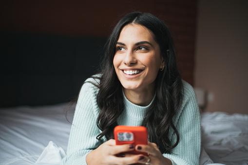 Smiling Woman relaxing in Bed using her Mobile Phone
