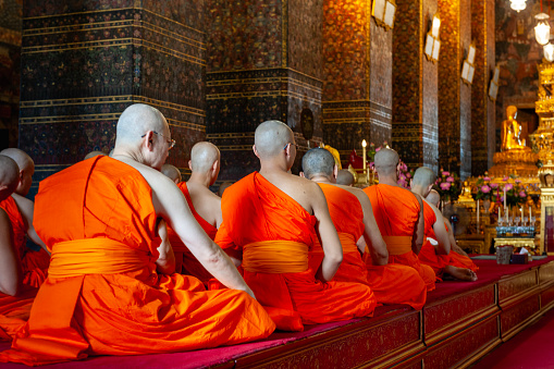 Buddhist monks and senior Thai people meditating and praying in the Buddhist temple Wat Arun in Bangkok Thailand, shot from the street