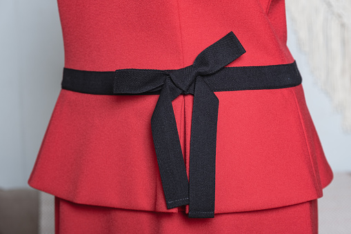 Black fabric belt with bow on a red women's dress. Elegant romantic women's clothing. Dress details.