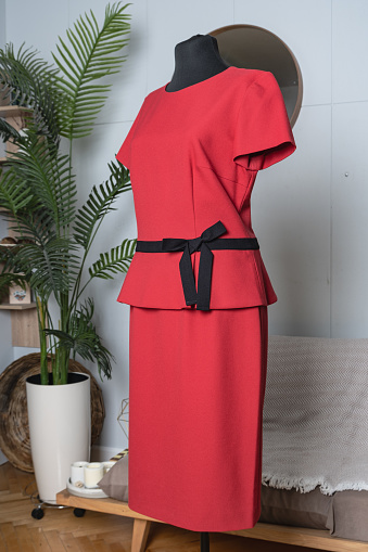 Elegant red dress with short sleeves and a black belt. Side view of a tailor's mannequin. Demonstration of women's clothing.