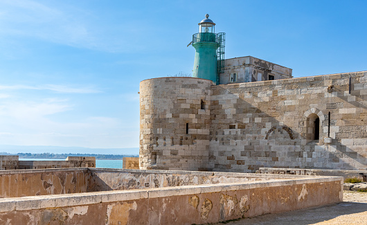 Syracuse, Sicily, Italy - February 16, 2023: Lighthouse over Castello Maniace Castle fortress walls and bastions at Ionian sea rocky shore on Ortigia island of Syracuse historic old town