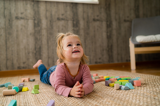 Full length of happy little girl is lying on the floor surrounded by toy blocks