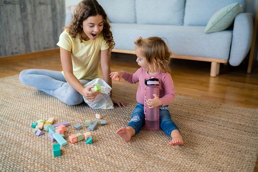 A teenage girl plays with toy block with her younger sister in the living room