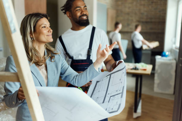 istock Smiling female architect and black worker making plans in moving apartment. 1839864989