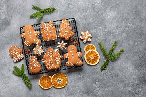 Various Christmas gingerbread cookies decorated with fir branches and orange slices, gray concrete background. Top view, flat lay, space for text.