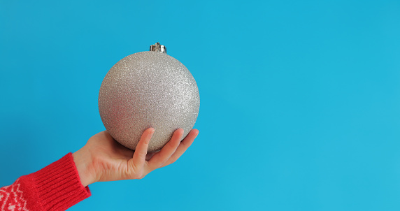 Large silver Christmas ball in a woman's hand, Christmas decoration, blue background, New Year. Christmas decor, Christmas tree toy close-up. Banner, copy space