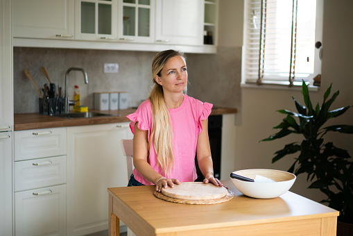 Happy blonde woman sitting in the kitchen whit cutting board and looking away