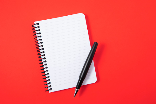 Notebook with pen on red background
