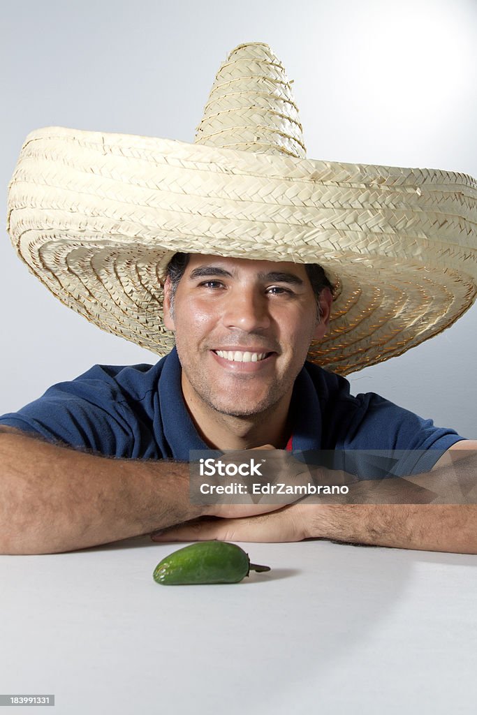 Uomo sorridente con cappello messicano e peperoncino sul tavolo - Foto stock royalty-free di Abbigliamento