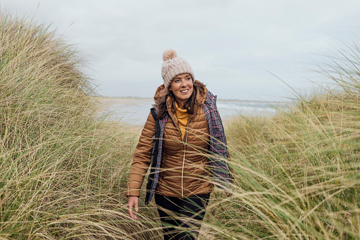 A front view medium close up of a mature woman who is exploring along the coast of Bamburgh in the North East of England. She is with a group of female friends and they are taking in the beautiful views.