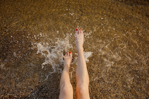 Close-up of joyful feet kicking in the clear, sunlit waters of the sea, capturing the essence of summer