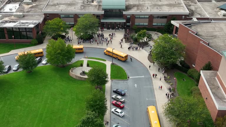 Students at public school campus buildings as school buses arrive to transport learners. Diversity DEI theme in American education. Aerial.