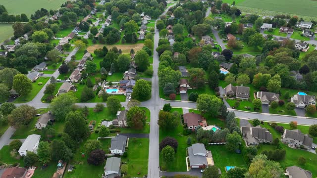 Aerial view of a lush, green suburban neighborhood with winding roads. Drone shot of American neighborhood in summer.