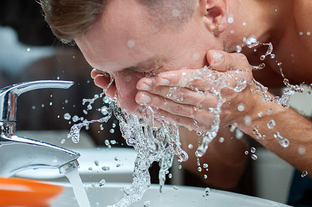 istock Man washing face over sink with faucet running  183995328