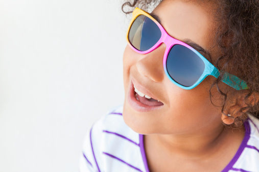 A beautiful and happy mixed race African American female girl child wearing sunglasses in bright sunshine on vacation shot with a white background