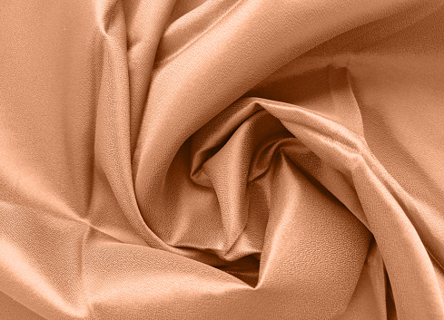 Peach fuzz is the color trend 2024. Silk fabric folded with beautiful curves with shadows, top view