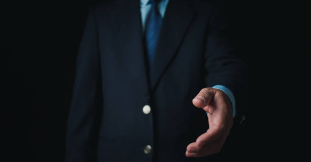 istock Businessman standing and doing handshake gesture on dark background. Business concept. Copy space. 1839977539