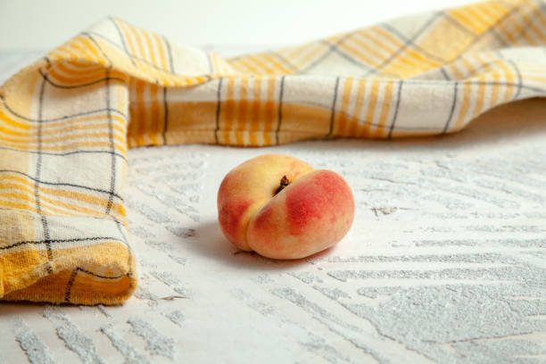 Ripe chinese flat peach fruit or saturn peach on vintage white wooden background with yellow kitchen towel.