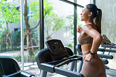 Asian Woman Doing Treadmill Run at an Indoor Fitness Gym Club, Sunshine Glowing Through Windows
