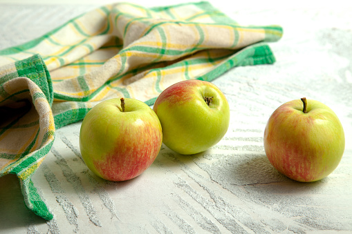 Three fresh green apples on white wooden background with green kitchen towel.
