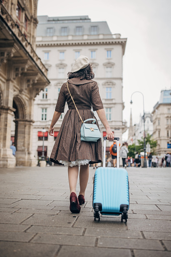 Modern young woman with carry-on luggage walking on the streets in Vienna.
