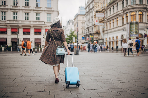 Modern young woman with carry-on luggage walking on the streets in Vienna.
