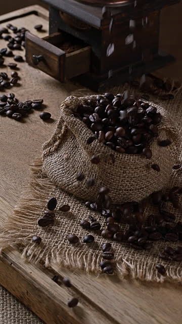 Slow motion of Coffee Beans falling into burlap sack on table in a rustic kitchen