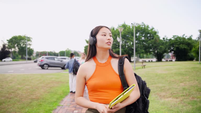 Asian student using headphones and mobile walking along the campus