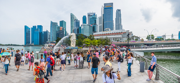 Crowds of tourists on the waterfront overlooked by the futuristic skyscraper cityscape of the Central Business District and Marina Bay Sands, Singapore.