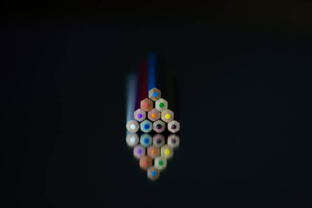 Color wooden crayons arranged in a triangular arrangement illuminated by a low light in the dark