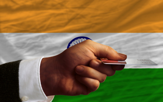 man stretching out credit card to buy goods in front of complete wavy national flag of india