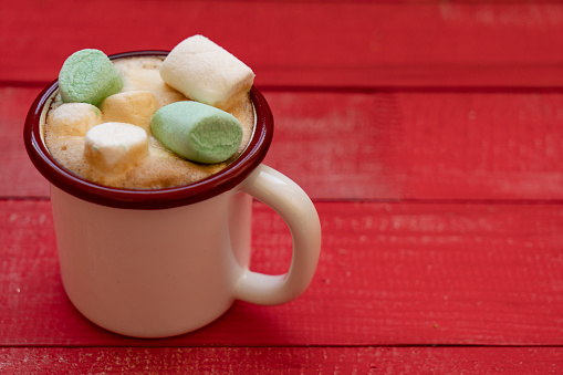 cup of hot cocoa with marshmallows on red wooden background