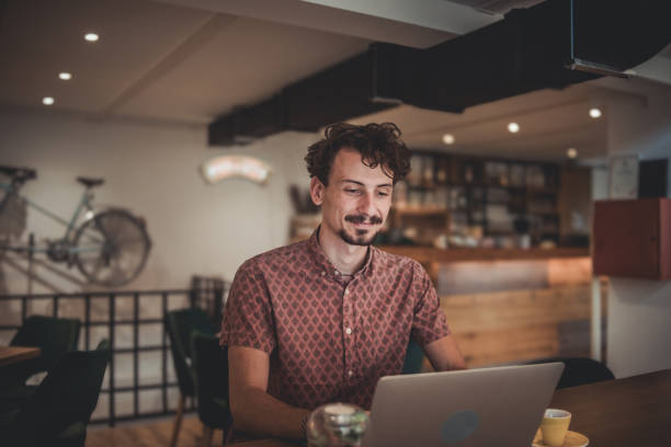 istock Young hipster man sitting in cafe drinking coffee and using digital device, laptop to surf internet or work online 1840102268