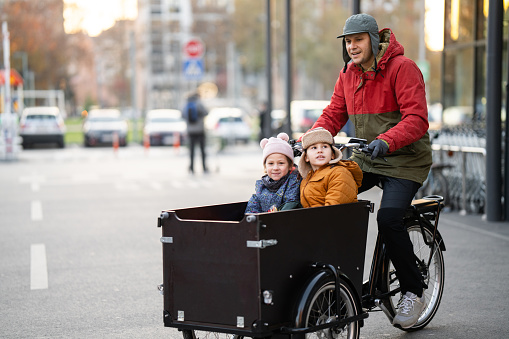 Happy father riding his two kids in cargo bike in the city