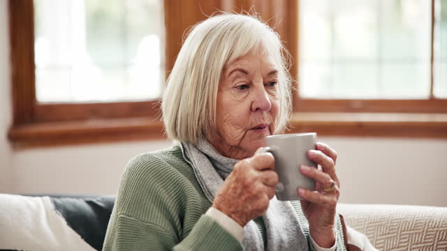 Coffee, thinking and senior woman relax on a sofa peaceful, calm or having a quiet morning in her home. Face, break and elderly lady person with tea in a living room resting or enjoying retirement