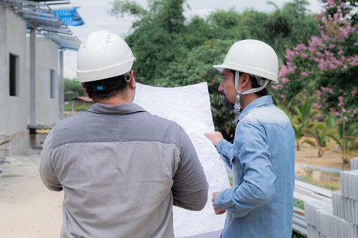Team of Asian foremen, or head engineers construction supervisors wearing white helmet hold  blueprint inspect building in workplace site, Professional supervisors discuss or solving problem concept