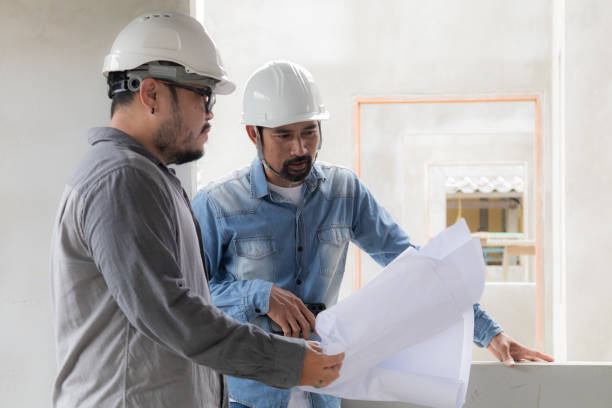 istock Young overweight engineering man wearing safety white helmet consulting with project manager partnership, Asian foreman fixing error control in construction site building holding blueprint paperwork 1840132433