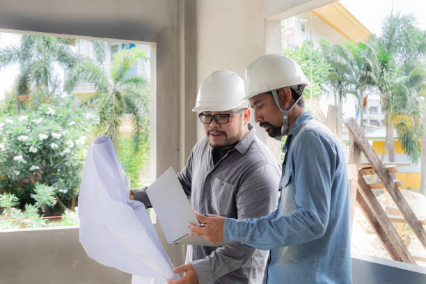 istock Hispanic engineer man with mustache wearing safety white helmet consult team project manager partnership, Asian foreman standing in construction site building reading blueprint and laptop technology 1840133471