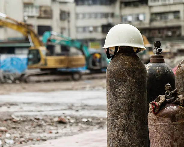 Hardhat on a gas cylinder at a construction site with rubble and trucks demolishing