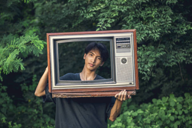 Young man holds old vintage TV frame outdoors in forest background.