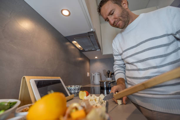 istock Man preparing healthy salad in the kitchen, following tutorial on digital tablet 1840210247