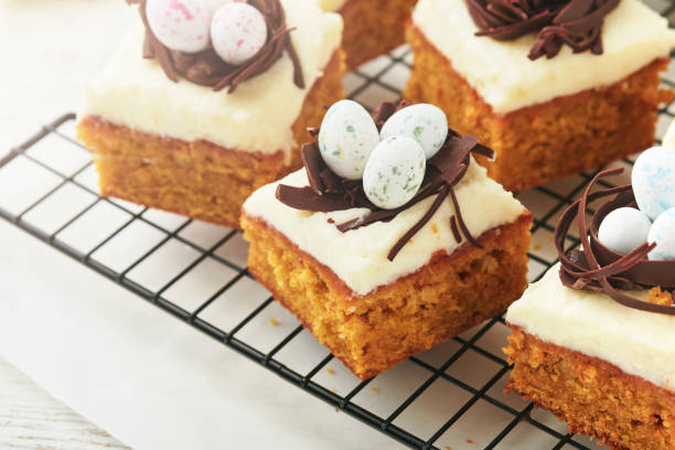 istock Easter carrot cake bars decorated with chocolate nest and chocolate candy eggs blossoming cherry or apple flowers on rustic light wooden backgrounds. Easter holiday meal. Traditional Easter food. 1840226441