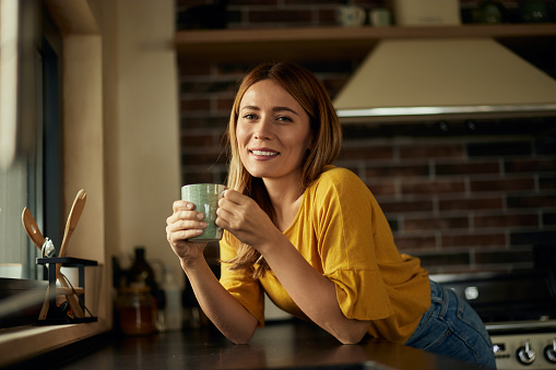 A beautiful blonde woman, enjoying her first-morning coffee, smiling for the camera.