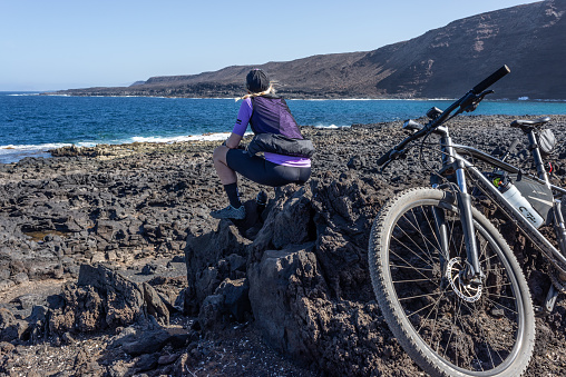 Young woman in cycling clothes enjoys a break from cycling at the coast of Lanzarote near La Santa