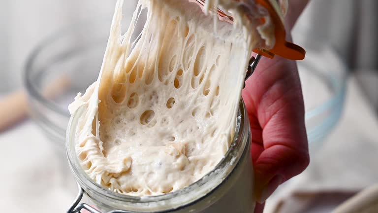 Sourdough starter in a mason jar glass, female hand opening a glass of wild yeast.