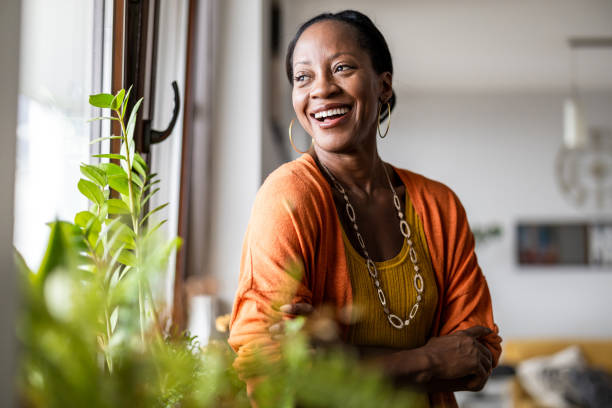 portrait of a smiling mature woman standing in her apartment - geluk stockfoto's en -beelden
