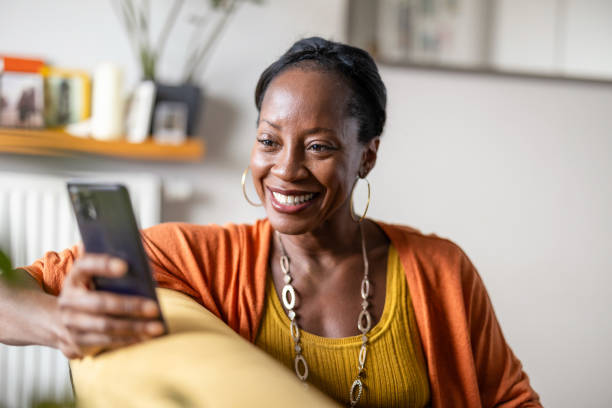 istock Mature woman using mobile phone while relaxing on a sofa at home 1840351878