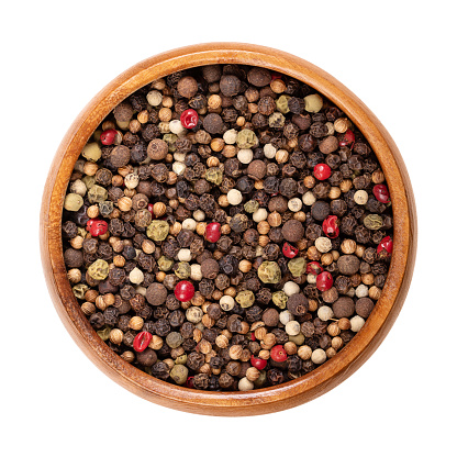 Piquant peppercorn mix in a wooden bowl. Spicy mixture of dried and whole black, green and white and peppercorns, rose pepper, coriander and allspice, to use in the pepper mill. Isolated, food photo.