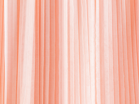 Abstract background of soft pleats of peach color quilled fabric. Festive background for design. A copy space. color trend 2024 Peach Fuzz.